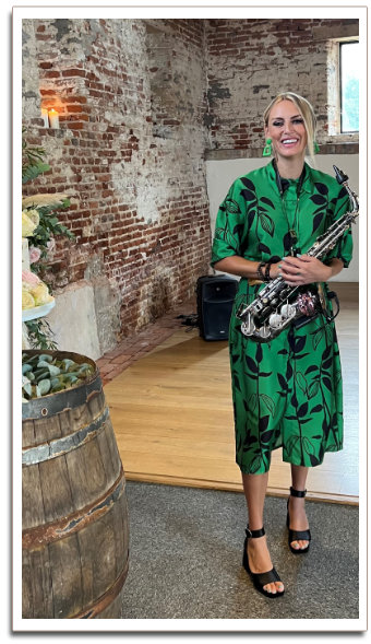 Kay wearing a green dress with black plant print stto lauging with Saxaphone in hand.